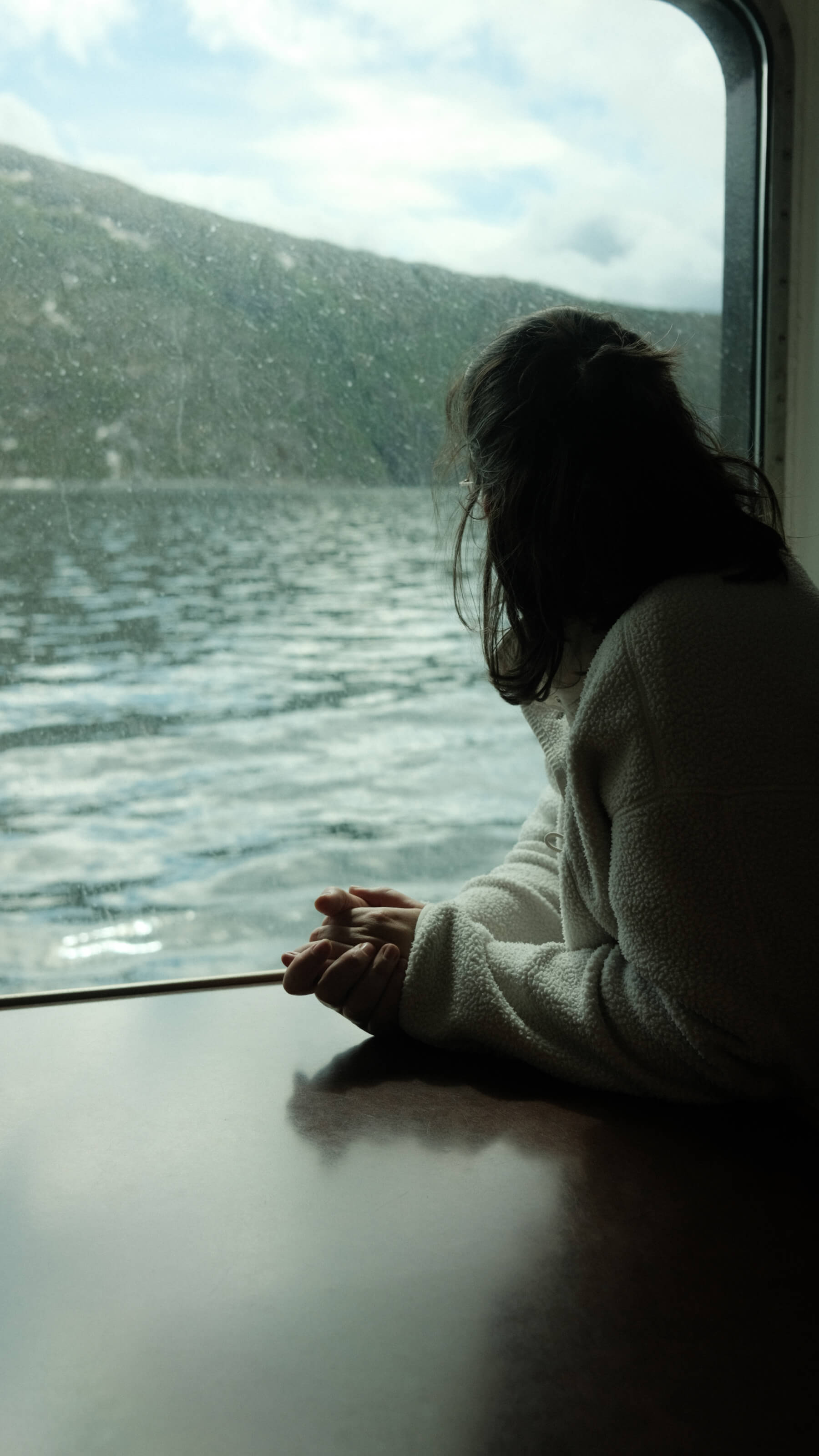 Frau blickt auf norwegischen Fjord durch Fenster auf Fähre